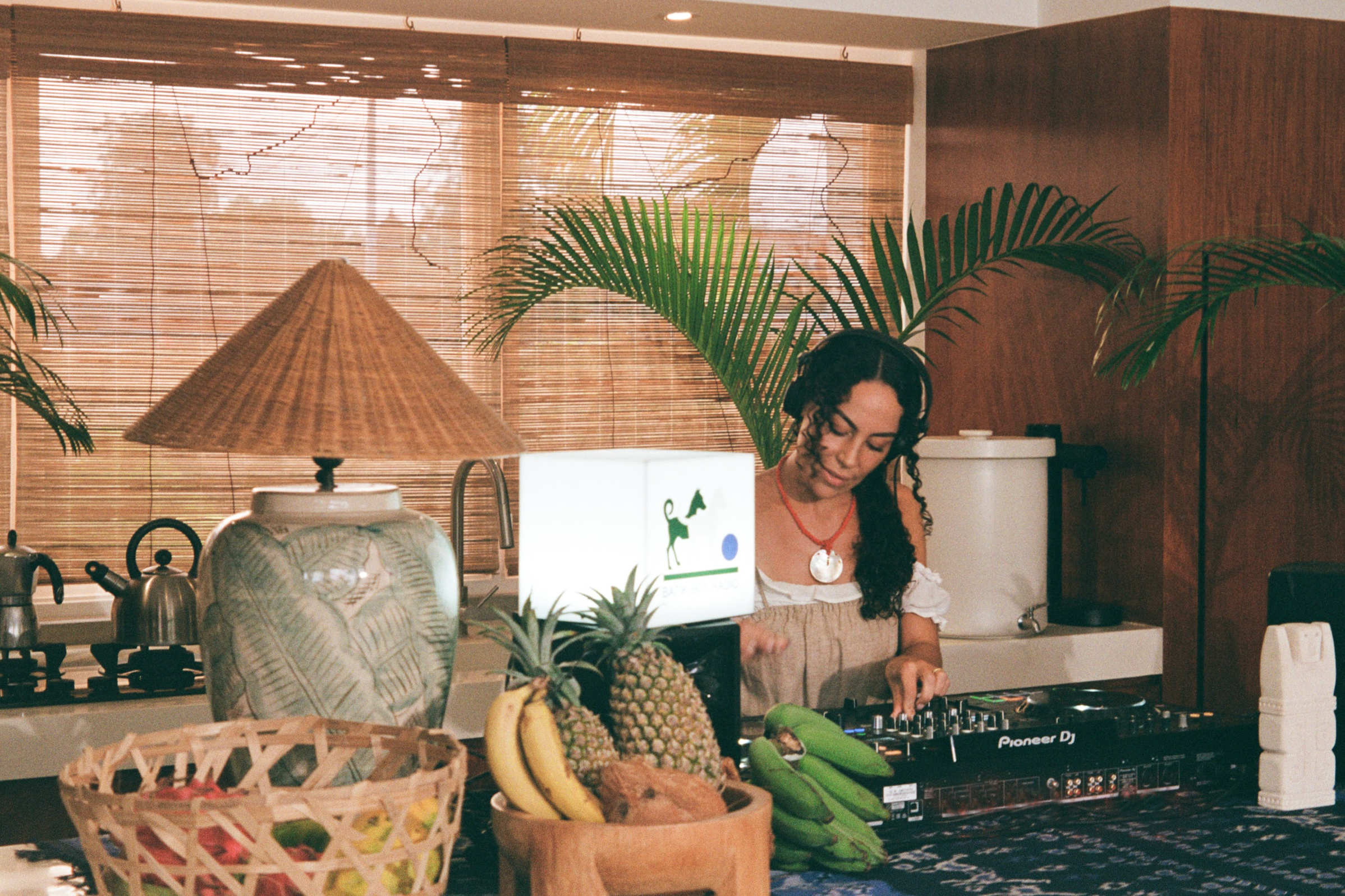 Woman using a DJ mixer in a kitchen with plants and kitchenware around