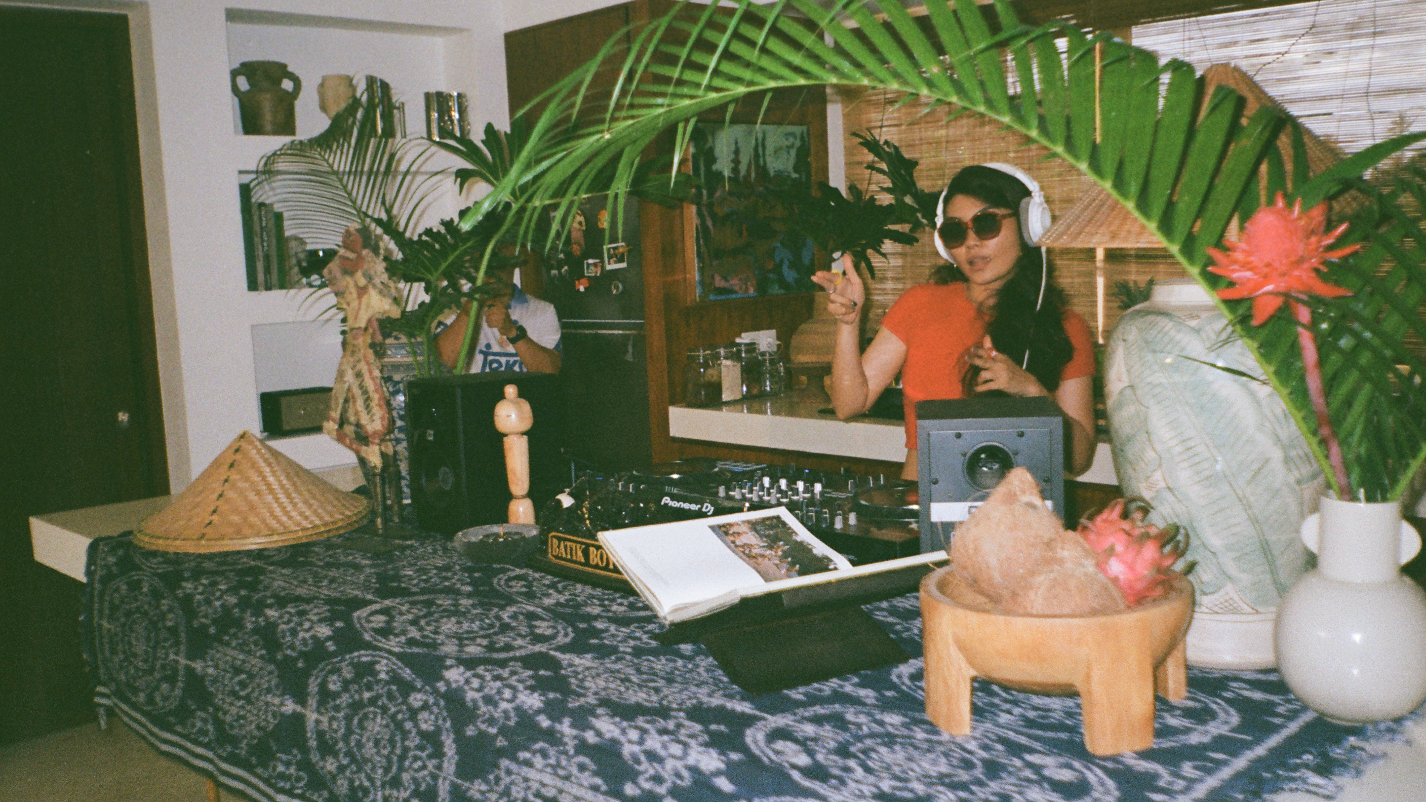 Person in a room with plants and DJ equipment, wearing headphones.