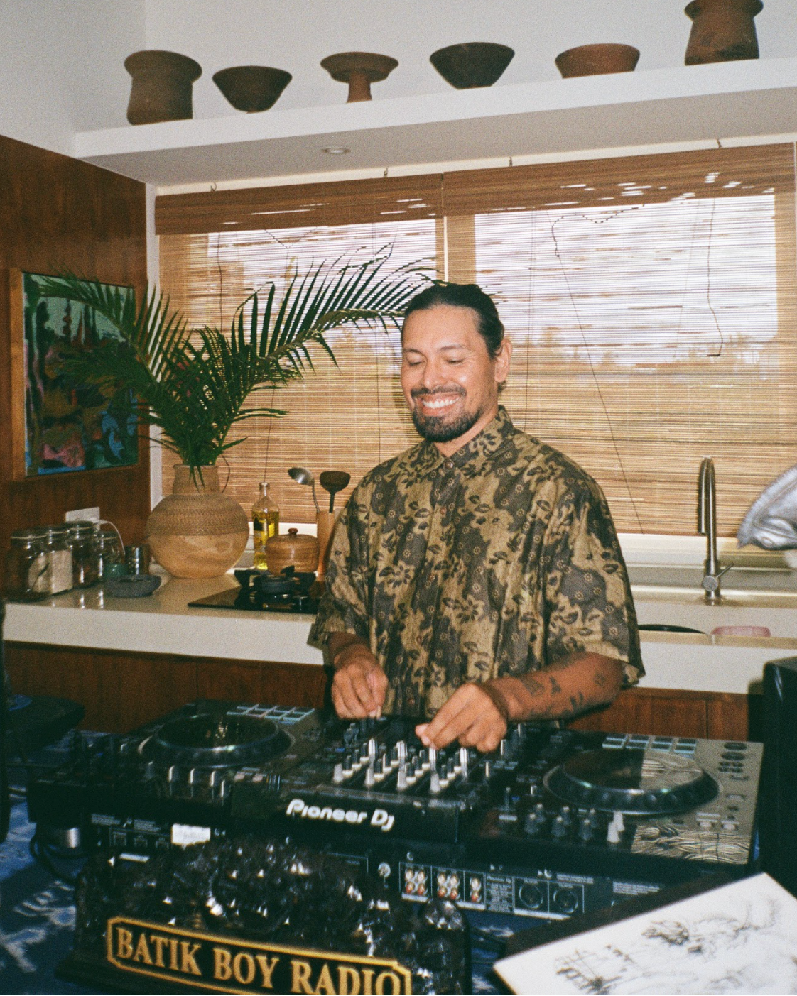 Man operating DJ equipment in a kitchen setting with decorative elements.